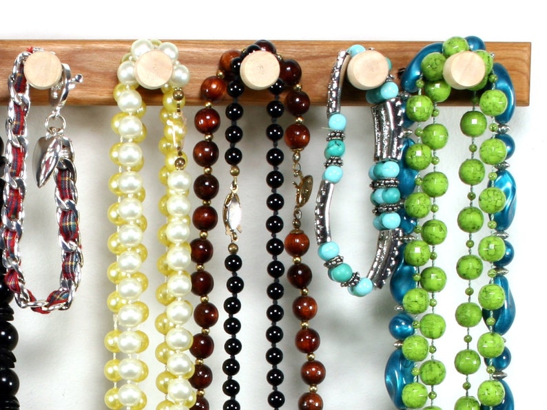 Puede incluir: Un estante de madera para joyas con varios collares y pulseras colgando de &eacute;l. Los collares est&aacute;n hechos de varios materiales, incluyendo perlas, cuentas y turquesa. Las pulseras est&aacute;n hechas de metal y turquesa.
