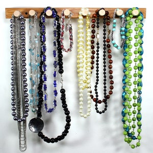 Puede incluir: Un estante de madera para joyas con nueve collares colgados. Los collares est&aacute;n hechos de varios materiales, incluyendo perlas, cuentas y metal. El estante es una excelente manera de organizar y exhibir joyas.