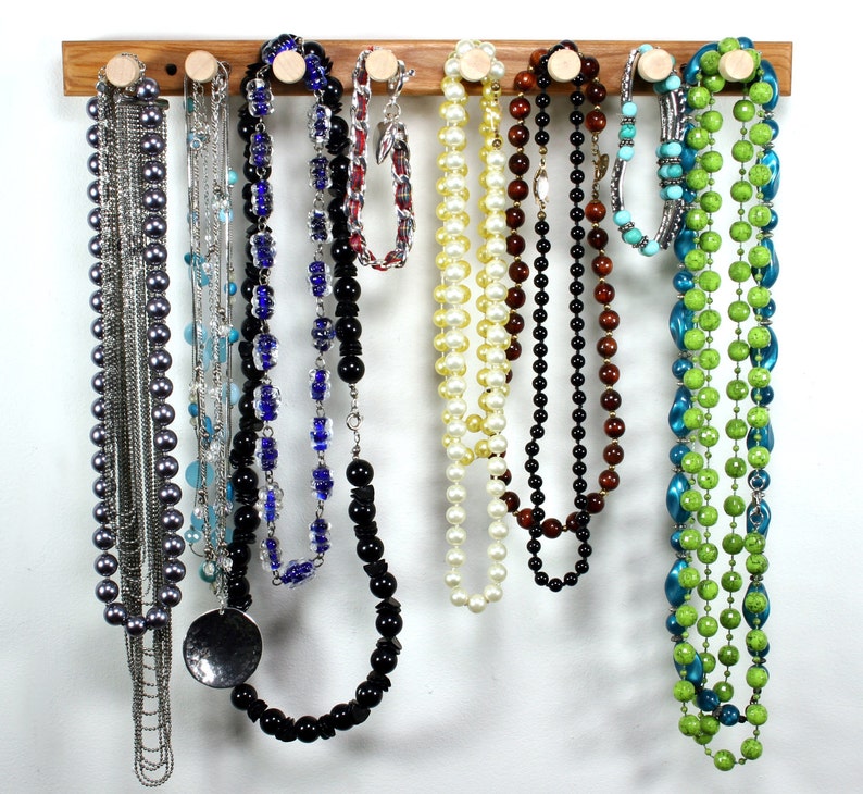 Puede incluir: Un estante de madera para joyas con nueve collares colgados. Los collares est&aacute;n hechos de varios materiales, incluyendo perlas, cuentas y metal. El estante es una excelente manera de organizar y exhibir joyas.