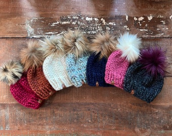May include: Seven knitted hats with faux fur pom poms in various colors, including red, orange, white, blue, navy, pink, and gray.