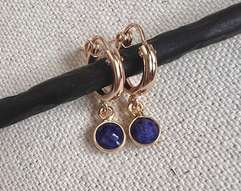 May include: Gold hoop earrings with a dangling blue gemstone. The earrings are simple and elegant.