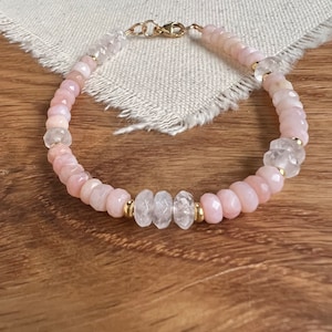 May include: A delicate bracelet made with pink opal and clear quartz beads, separated by gold spacers. The bracelet is strung on a gold chain with a lobster clasp.