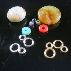 May include: A collection of colorful beads and metal jump rings. The beads are made of various materials, including stone, glass, and metal. The jump rings are silver and gold in color.