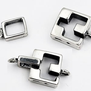 May include: Three silver-toned square jewelry clasps. One is a simple square with a loop, and the other two are square with a unique interlocking design and loops. The clasps are shown against a white background.