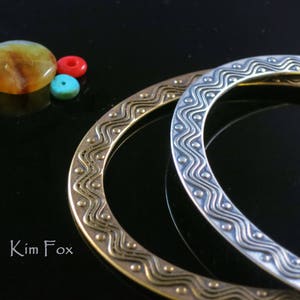 May include: Two metal rings with a wavy pattern. The ring on top is silver and the ring on the bottom is gold.