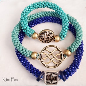 May include: Three beaded bracelets in shades of blue and turquoise with gold and silver metal charms. The charms feature Celtic knot designs.