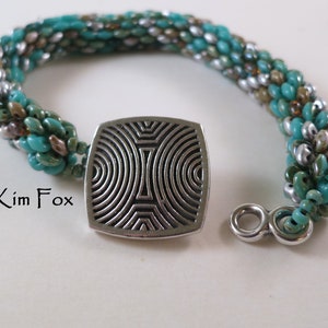 May include: A turquoise, silver, and brown beaded bracelet with a silver square-shaped clasp featuring a geometric design.  The bracelet is made with seed beads and has a silver toggle clasp.