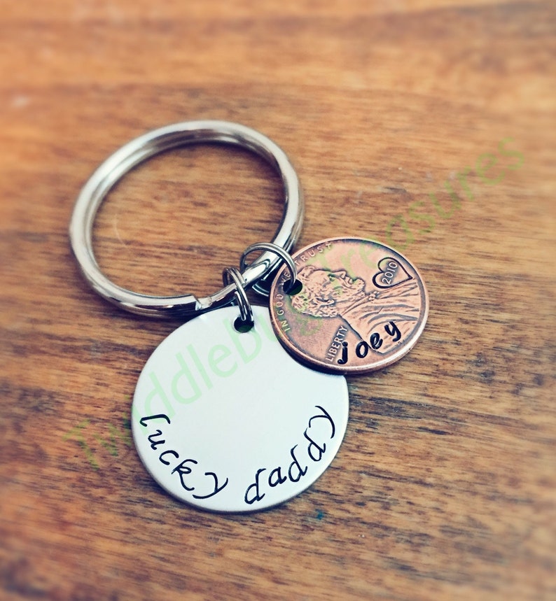 Pode incluir: Um chaveiro de prata com um charme redondo de prata que diz "lucky daddy" e uma moeda de cobre de um centavo com o ano 2010 e o nome "Joey" gravado nela.