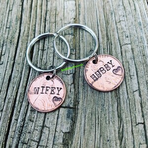 May include: Two copper penny keychains with silver key rings. The pennies have the words "WIFEY" and "HUBBY" engraved on them. The pennies are dated 2013.
