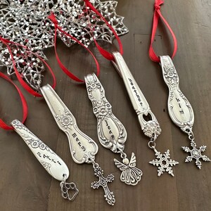 May include: Five silver spoon ornaments with red ribbon and charms. The spoons are engraved with the names "Mary", "Jean", "Heather", "Kim", and "Patti". The charms include a cross, an angel, a snowflake, a snowflake, and a paw print.