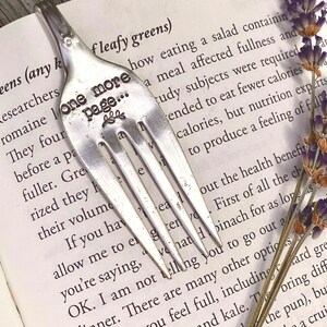 May include: A silver fork with the words "One more page..." engraved on the handle. The fork is resting on a page of a book with text about leafy greens.