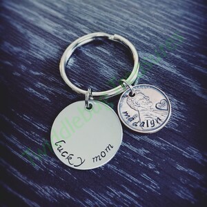 Pode incluir: Um chaveiro de prata com um charme redondo que diz "lucky mom" e um centavo de cobre com o ano 2010 e o nome "madalyn" gravado nele.