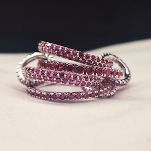 May include: A collection of silver rings, each encrusted with small, vibrant red gemstones. The rings are intertwined, creating a layered and textured appearance. The gemstones are closely set, enhancing the overall sparkle.