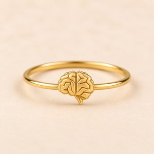 May include: A gold-toned ring featuring a small, detailed anatomical brain charm centered on a thin, smooth circular band. The brain charm displays a textured, segmented surface design that mimics the appearance of cerebral lobes.