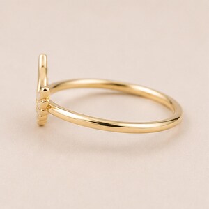 K&ouml;nnte beinhalten: Ein goldfarbener Ring mit filigranem Design. Der Ring hat ein schlankes Band und ein dekoratives Element, m&ouml;glicherweise eine stilisierte Hand oder ein Symbol. Der Ring wird vor einem neutralen Hintergrund pr&auml;sentiert, um seine polierte Oberfl&auml;che hervorzuheben.