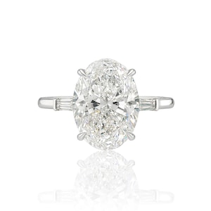 May include: A sparkling diamond ring with an oval-cut center stone and two smaller baguette diamonds on either side. The ring is set in a silver band, reflecting light and creating a brilliant display. The ring is a symbol of luxury and commitment.