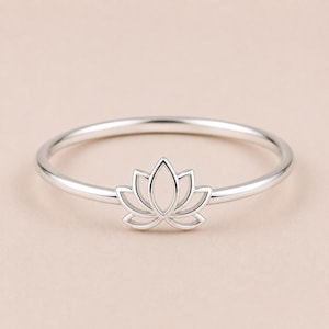 May include: A silver ring with a lotus flower motif. The ring has a slender band and a detailed lotus flower design. The ring is made of a shiny metal, and the lotus flower is the main focus of the piece.