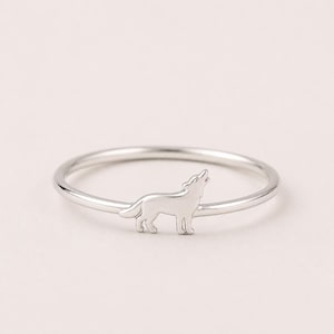 May include: A silver ring featuring a howling wolf silhouette. The ring has a thin band and a detailed wolf design, perfect for animal lovers. The ring is a delicate piece of jewelry.