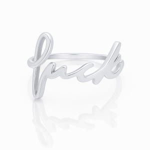 May include: A silver ring with the word "fuck" in a cursive font. The ring is displayed on a white background, with a reflection visible below.