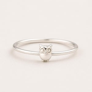 Peut inclure: Une bague fine en métal argenté poli ornée d'un petit motif de hibou centré. Le design du hibou comprend deux yeux circulaires, un petit bec pointu et des oreilles arrondies, intégrés harmonieusement à l'anneau lisse et circulaire.