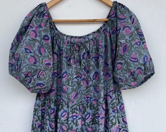 May include: A light blue dress with a floral pattern in shades of pink, purple, and green. The dress features short, puffed sleeves and a tiered skirt. The fabric appears to be lightweight, suitable for warm weather.