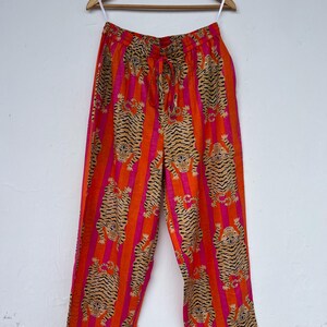May include: Orange and pink striped pants with a tiger print. The pants are hanging on a wooden hanger. The pants have a drawstring waist and a loose, comfortable fit. The tiger print is in shades of brown and black.