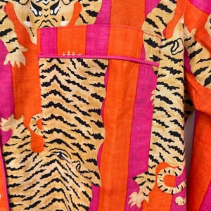 May include: Close-up of a vibrant pajama top featuring a tiger print and vertical stripes in orange, pink, and fuchsia. The pocket is outlined in pink. The tiger print includes black stripes on a tan background.