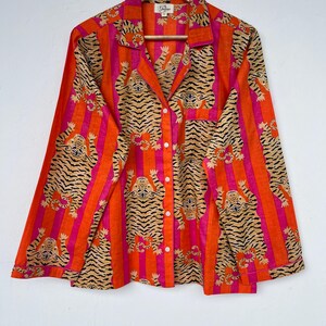 May include: A long-sleeved button-down shirt with a vibrant tiger stripe pattern. The shirt features vertical stripes in orange and pink, with tiger illustrations in tan and black. It has a collared neckline and a chest pocket.