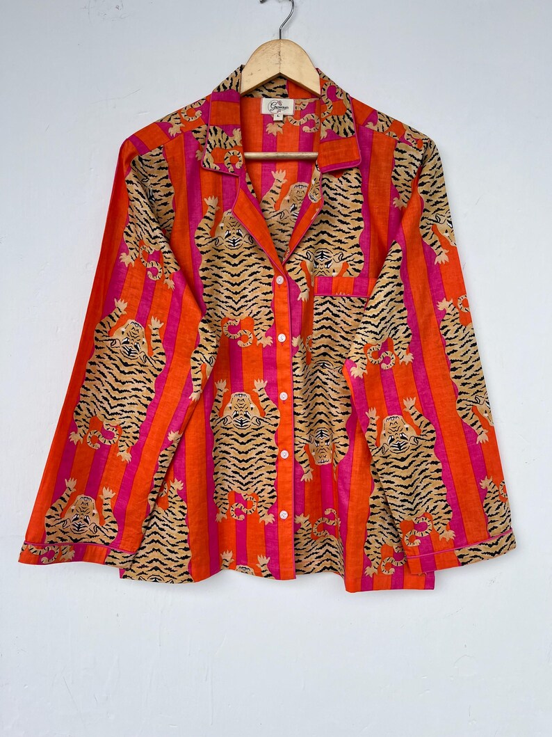 May include: A long-sleeved button-down shirt with a vibrant tiger stripe pattern. The shirt features vertical stripes in orange and pink, with tiger illustrations in tan and black. It has a collared neckline and a chest pocket.