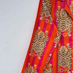May include: Orange and pink striped pajama top with a tiger print. The long-sleeved shirt features a collared neckline and button-down front. The tiger print is in a tan and black color.