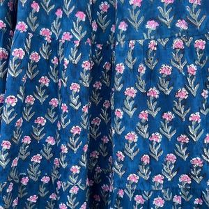 May include: A tiered, dark teal fabric with a repeating floral pattern. The flowers are pink with gray-green stems and leaves. The fabric appears to be a dress or skirt.