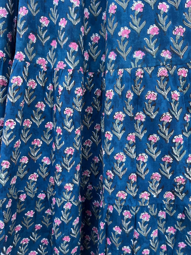 May include: A tiered, dark teal fabric with a repeating floral pattern. The flowers are pink with gray-green stems and leaves. The fabric appears to be a dress or skirt.
