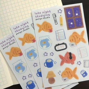 May include: Sheets of stickers with a late-night studying theme. The stickers feature goldfish, fishbowls, a window with a moon and stars, a pencil, a pen, a clock, a teacup, a lamp, and the text "late night studying ponyu studio."