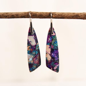 Può includere: Un paio di orecchini pendenti dal design unico e colorato. Gli orecchini presentano un mix di pietra viola, verde acqua e color crema, con un gancio color argento. Gli orecchini sono appesi a un ramo marrone su sfondo bianco.