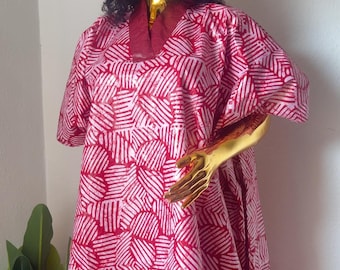 May include: A red and white patterned dress and matching head covering are displayed on a mannequin. The dress has short sleeves and a V-neck. The fabric features a repeating geometric design. The mannequin has a gold head and arm.