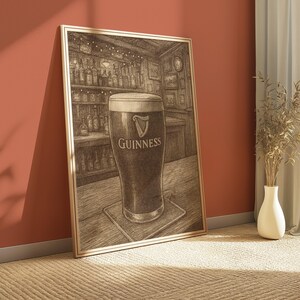May include: A framed sepia-toned print of a pint of Guinness stout in a pub setting. The glass is centered on a wooden bar, with the Guinness logo visible. The background shows shelves of bottles and a clock.