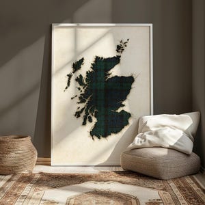 May include: A framed print depicting the outline of Scotland, filled with a green and navy tartan design. The artwork is set against a cream backdrop and framed in white. The room includes a woven basket, a patterned rug, and a beige ottoman.