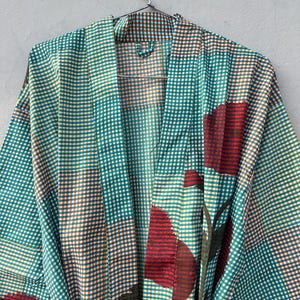 May include: A teal, brown, and white checkered robe with large red floral accents. The robe is hanging on a metal hanger against a neutral background. The robe's pattern is a mix of small checks and large floral designs.