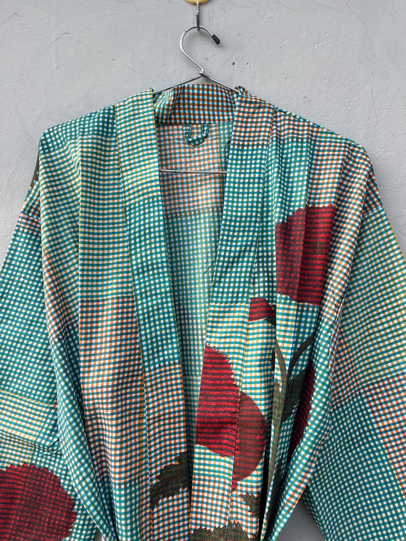 May include: A teal, brown, and white checkered robe with large red floral accents. The robe is hanging on a metal hanger against a neutral background. The robe's pattern is a mix of small checks and large floral designs.