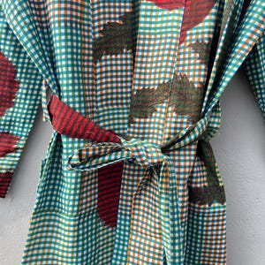 May include: A colorful robe with a gingham pattern in teal, orange, and white. The robe features a tie belt and is adorned with leaf and floral designs in red and green. The fabric appears to be lightweight, suitable for lounging.