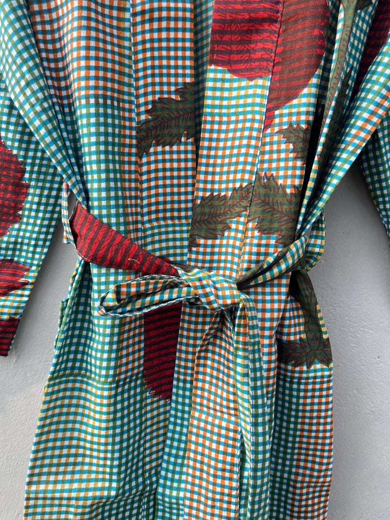 May include: A colorful robe with a gingham pattern in teal, orange, and white. The robe features a tie belt and is adorned with leaf and floral designs in red and green. The fabric appears to be lightweight, suitable for lounging.