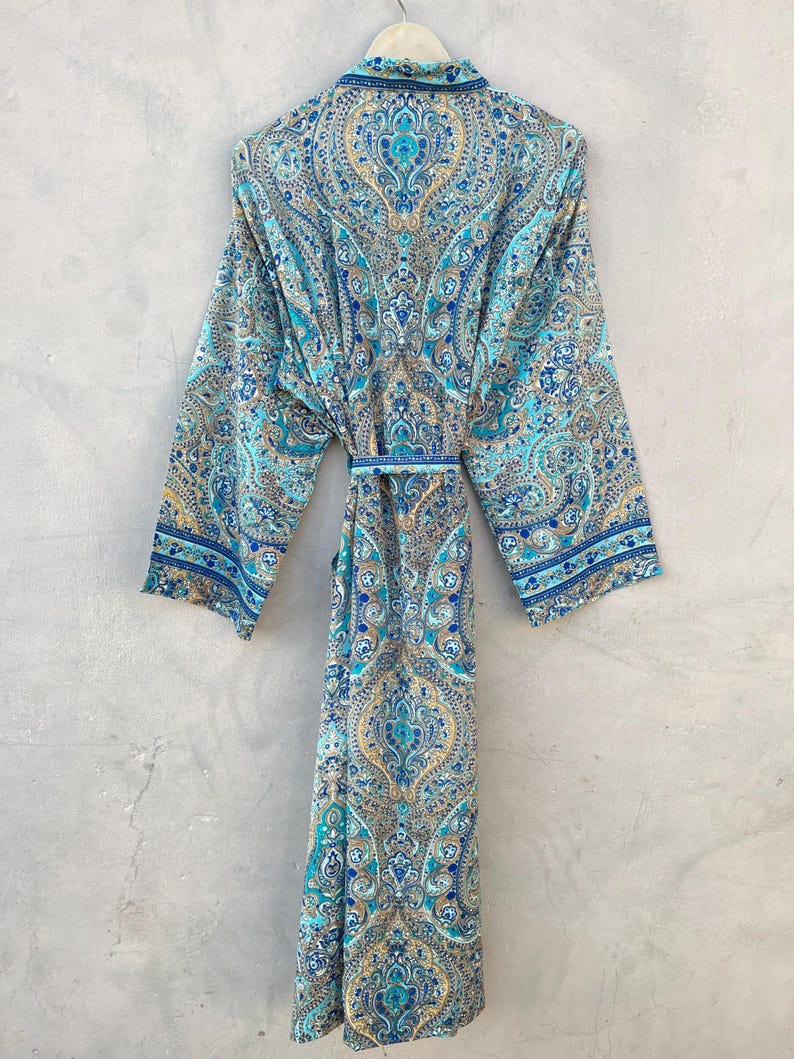 May include: A long, flowing robe with a vibrant paisley pattern in shades of blue, teal, and gold. The robe features long sleeves, a collared neckline, and a matching belt. The garment is hanging on a hanger against a neutral gray background.