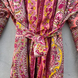 Puede incluir: Una bata con estampado de cachemira en tonos rosa, amarillo y morado. La bata est&aacute; atada a la cintura con un cintur&oacute;n a juego. La tela presenta un dise&ntilde;o floral detallado y rayas verticales. Las mangas son visibles a ambos lados de la bata.