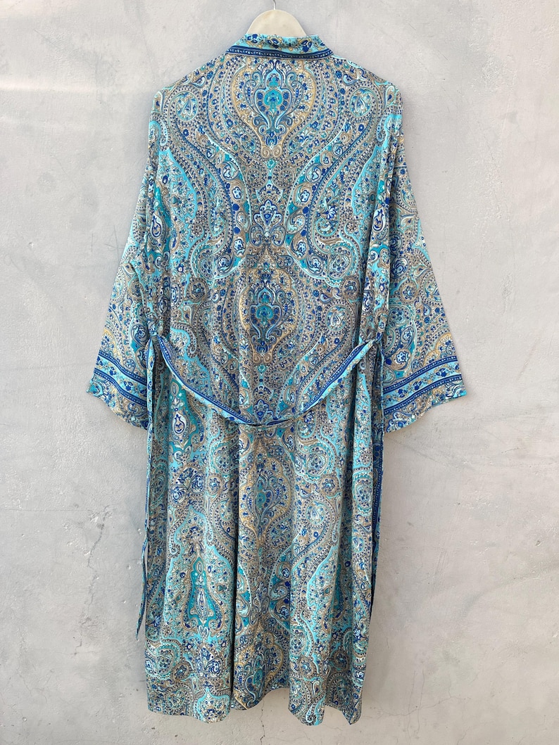 May include: A long, flowing robe with a paisley pattern in shades of blue, teal, and gold. The robe has long sleeves, a collar, and a matching belt. The garment is hanging against a neutral gray background.
