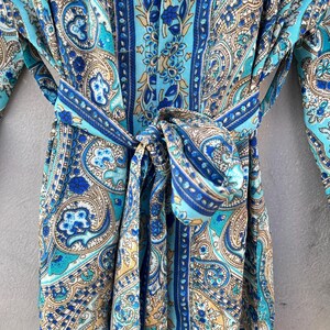 May include: A blue paisley patterned robe with a matching belt tied in a bow. The robe features shades of blue, teal, and tan. The fabric has a silky appearance and a detailed floral design.