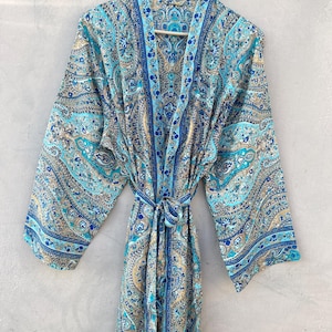 May include: A long, flowing robe with a paisley pattern in shades of blue, teal, and gold. The robe has wide sleeves and a matching tie belt. The garment is hanging on a wooden hanger against a neutral background.