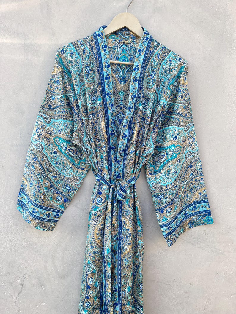 May include: A long, flowing robe with a paisley pattern in shades of blue, teal, and gold. The robe has wide sleeves and a matching tie belt. The garment is hanging on a wooden hanger against a neutral background.