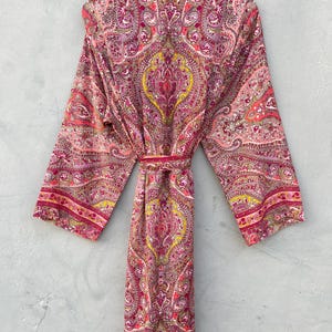 Puede incluir: Bata larga con frente abierto, con un estampado de cachemira en tonos rosa, rojo y amarillo. La bata tiene mangas largas y un cintur&oacute;n a juego. La tela ligera es adecuada para descansar o como prenda de abrigo.