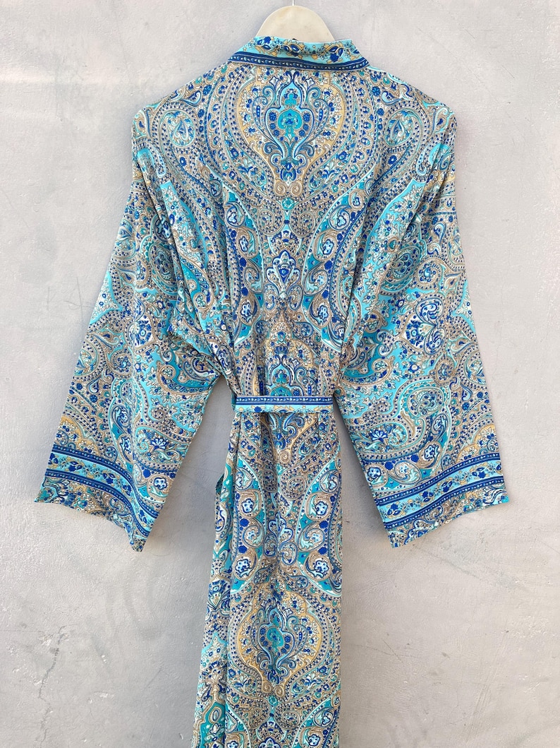 May include: A long, flowing robe with a vibrant paisley pattern in shades of blue, teal, and gold. The robe features wide sleeves and a matching belt. The fabric appears lightweight and suitable for warm weather.