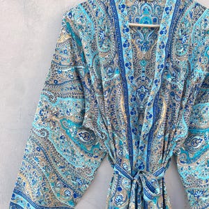 May include: A blue paisley patterned robe with a matching tie belt. The robe features shades of blue, teal, and tan. The robe is hanging on a wooden hanger against a neutral background.